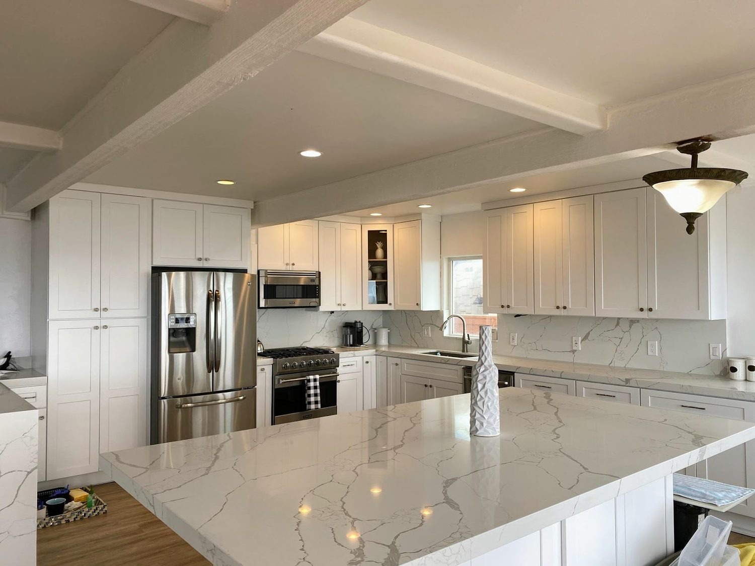 A finished kitchen with white shaker cabinets, stainless appliances and a large island topped in veined white quartz.