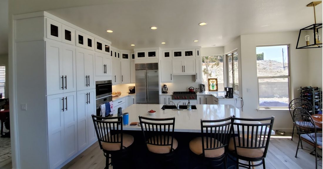 A kitchen with floor-to-ceiling white cabinetry, glass-front upper cabinets and a long island with dining chairs.