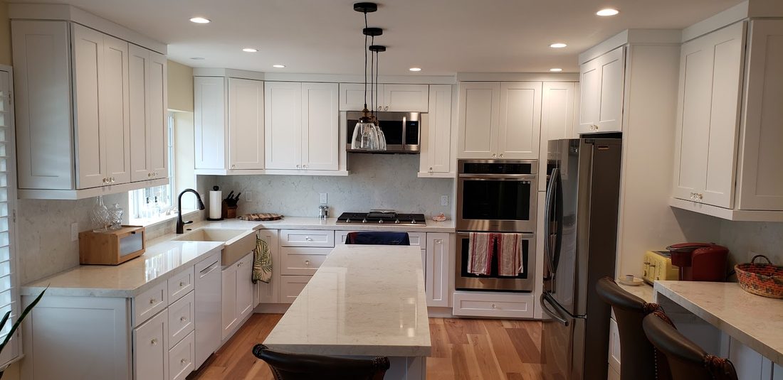 A white kitchen with a wood floor running through it, a range and an island with a prep sink.