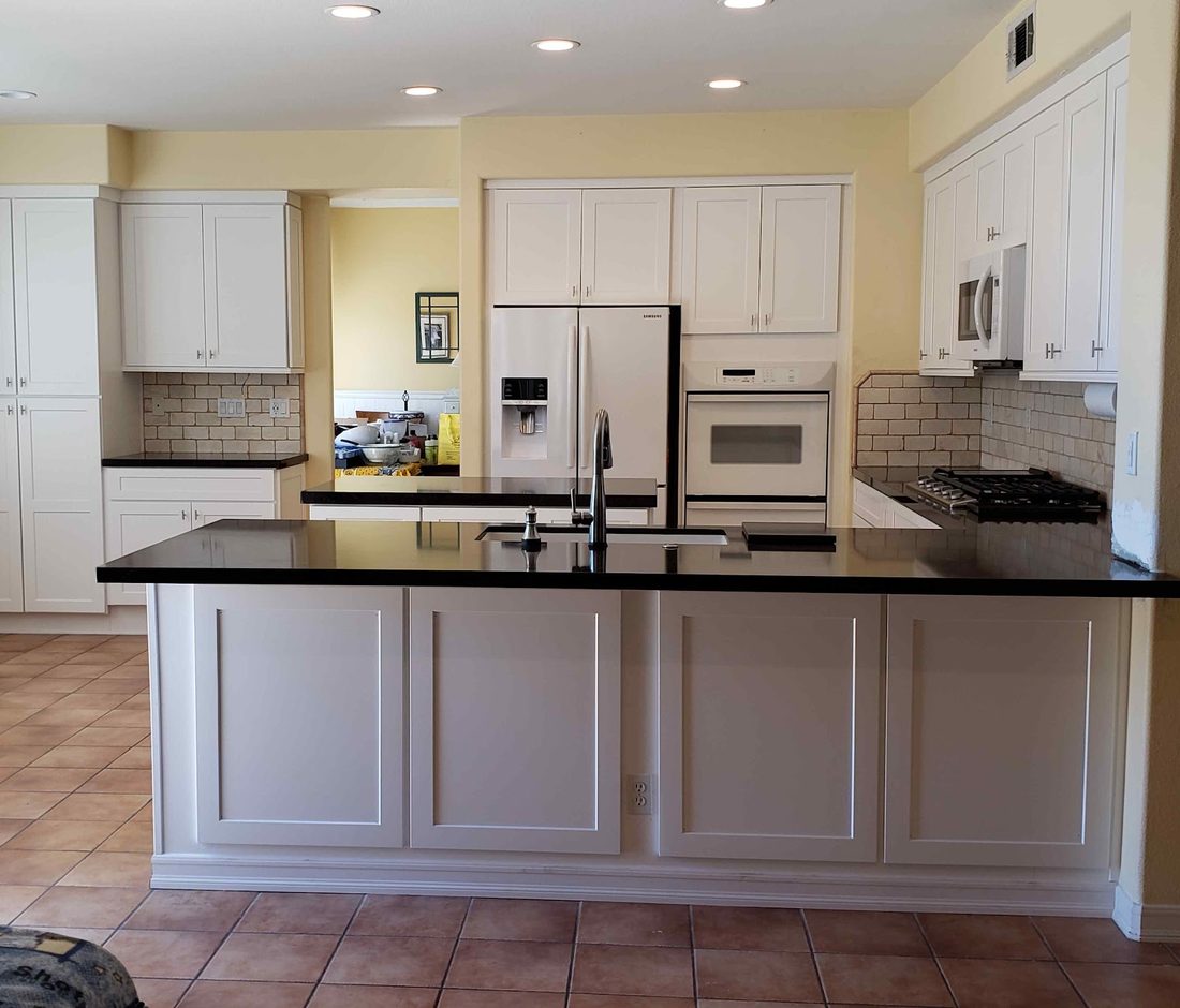 A kitchen with white cabinets, black granite countertops and a tiled backsplash above the range.